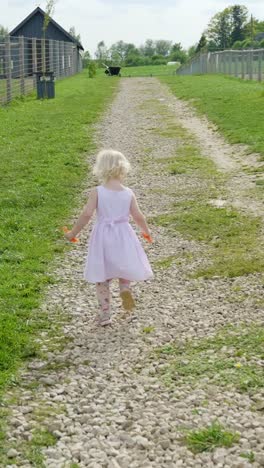 a small girl runs in slow motion along a fenced path at the zoo on a sunny day