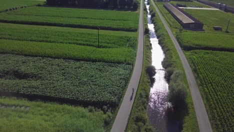 aerial view of a young man riding a bicycle in sugana valley, italy with camera tilting down as biker rides through the road