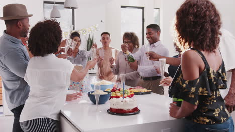 Hombre-Negro-De-Mediana-Edad-Abriendo-Champán-Y-Sirviéndolo-Durante-Una-Celebración-En-Casa-Con-Su-Familia