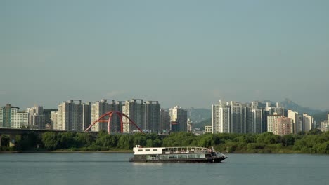 ferry cruise ship traveling on han river along bamseom island with seoul urban high-raised apartment buildings, seogang bridge and bukhansan mountains on background, tourism in south korea autumn