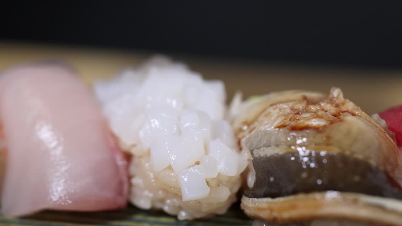 木製の板に載った、マグロやウナギを含むさまざまな握り寿司のマクロショット
