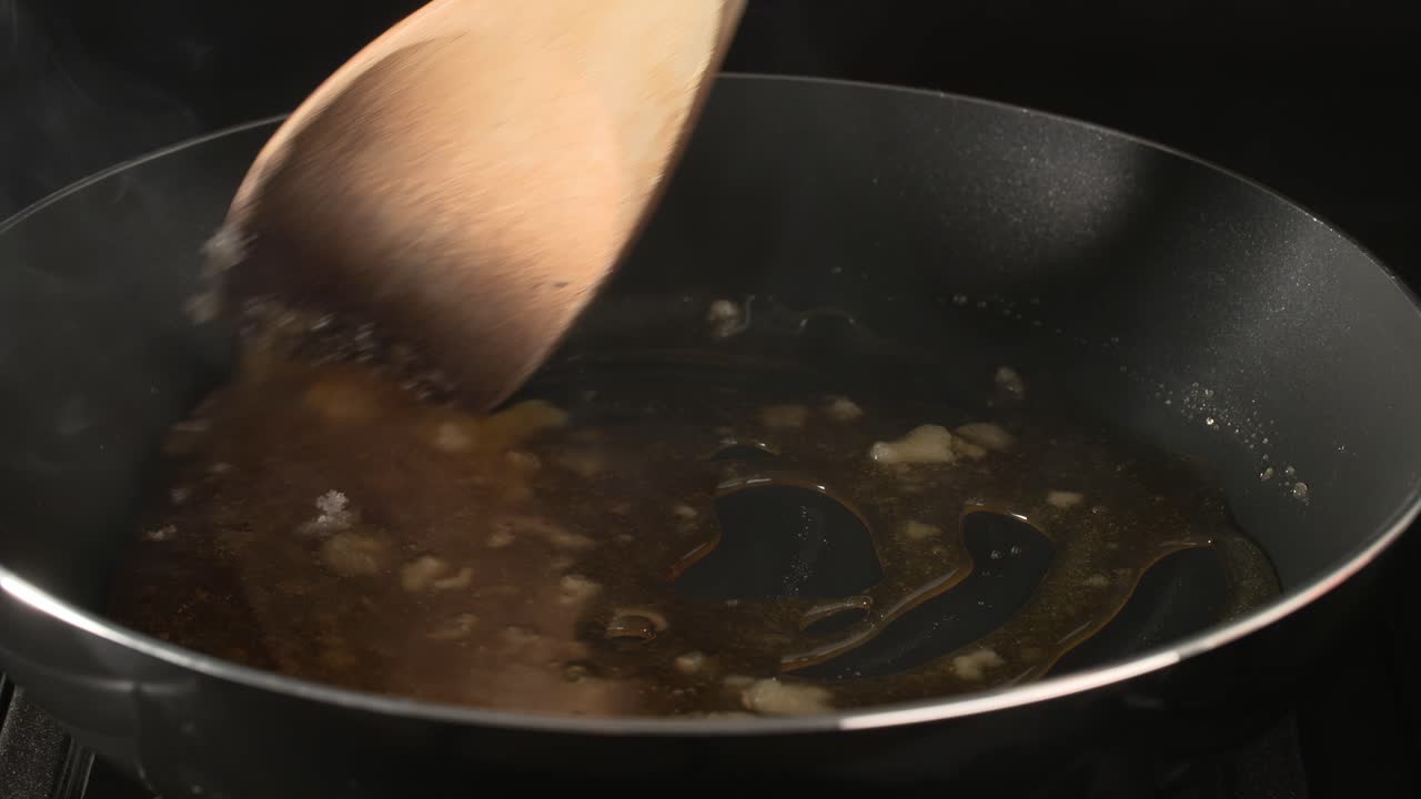 Melting sugar and mixing caramel with a wooden spoon in a pan on Gas stoves on a black background