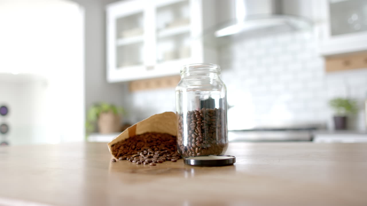 Coffee beans spilling from paper bag into glass jar on kitchen counter