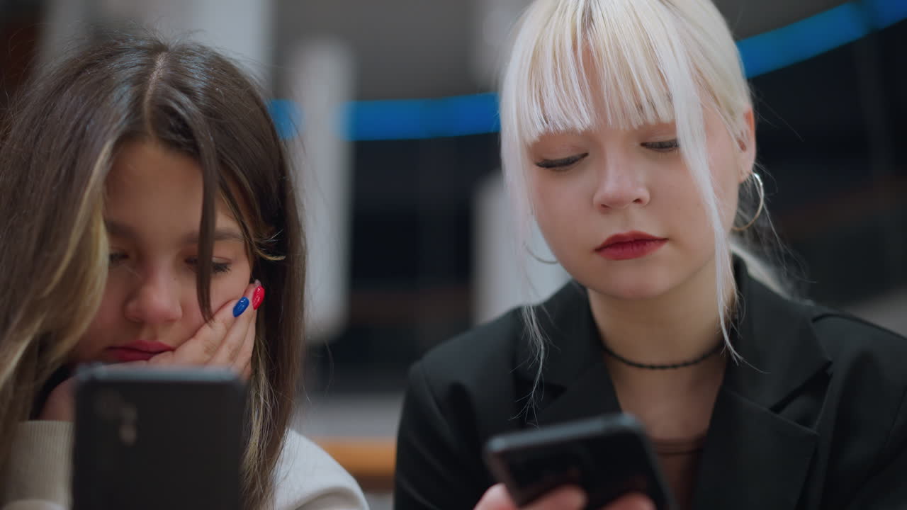 Close up view of high school girls operating phone while chatting indoors showing serious expressions reflecting digital lifestyle, communication and social interaction