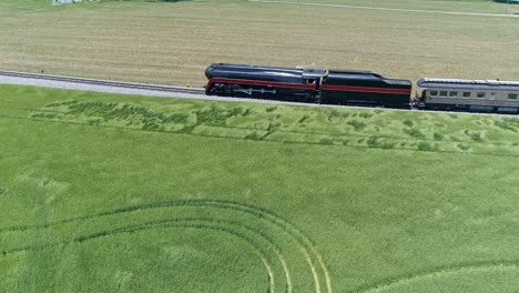 an aerial parallel view of an antique steam passenger train traveling thru farmlands on a sunny day