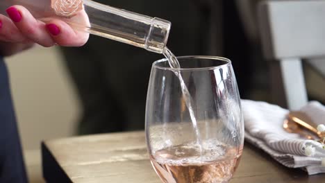 vin de rose versé dans un verre à vin sans pied et ramassé de la table à servir, gros plan de la main d'une femme portant du vernis à ongles rose et une serviette de cuisine en arrière-plan, couleur rouge blanc et doré