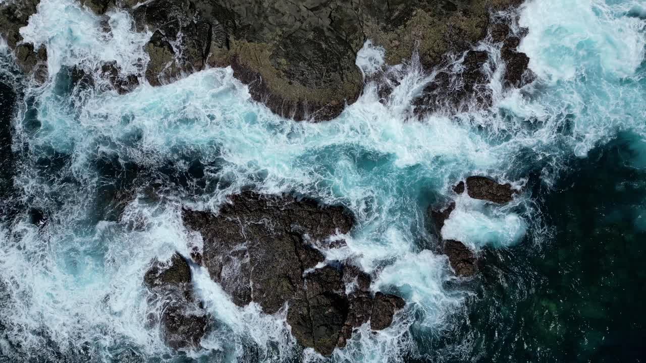 Vista aerea da drone che mostra le onde che si infrangono su una costa rocciosa.
