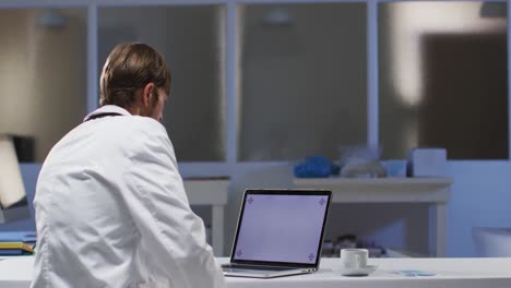 médico caucásico que tiene una consulta de videollamada usando una computadora portátil