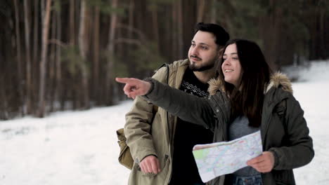 caucasian couple checking map for directions in a snowed forest.