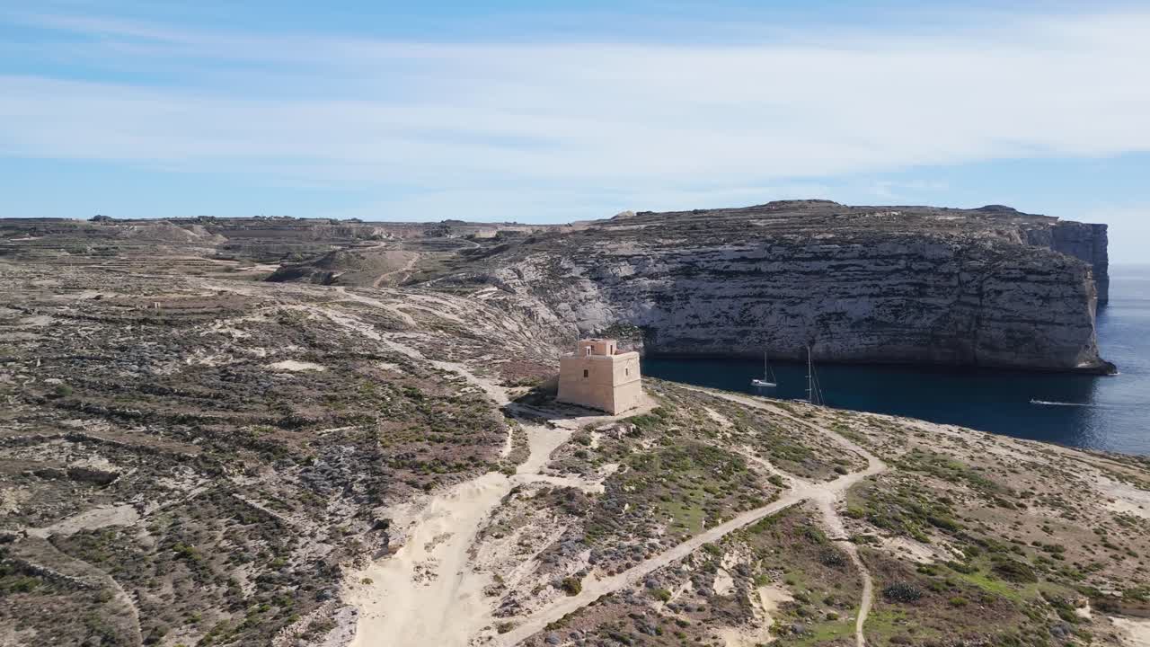 Ripresa aerea con drone del Castello di Dwejra a Gozo, Malta, filmato cinematografico in 4K a 60 FPS che mette in mostra la storica torre in pietra calcarea, la costa spettacolare e il paesaggio mediterraneo