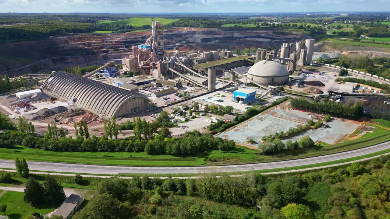 A drone pullback shot reveals the cement factory in Saint-Pierre-la-Cour, with the quarry in the background, a road in the foreground, and surrounding vegetation
