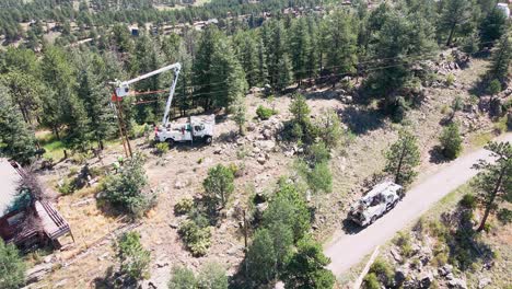 vista aérea de un equipo de servicios públicos que usa un camión de cubeta para trabajar en un poste de energía en un vecindario montañoso remoto