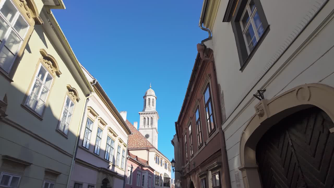 Walk in the historic old town of Sopron, where the tower of the Evangelical Parish Church rises above the classical houses with blue sky background in Hungary.
