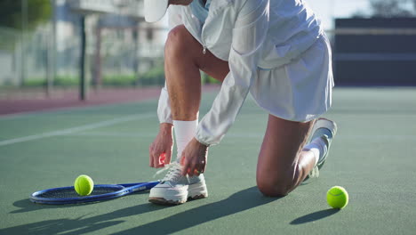 woman tying shoelaces on tennis court