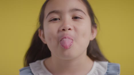 studio portrait of hyperactive girl smiling and pulling faces against yellow background 2