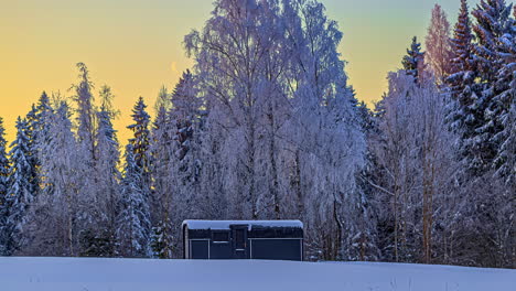 Thermoholz-Hüttenhaus-In-Verschneiter-Winterlandschaft-Mit-Aufgehendem-Mond-Bei-Farbenprächtigem-Sonnenaufgang-Am-Morgen---Zeitrafferaufnahme