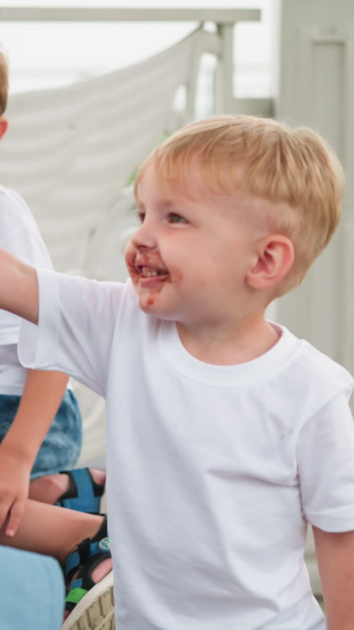 мать и ее двое маленьких детей, младший мальчик, лицо покрытое шоколадом, предлагает свой мороженое своей матери, в то время как старший ребенок смотрит