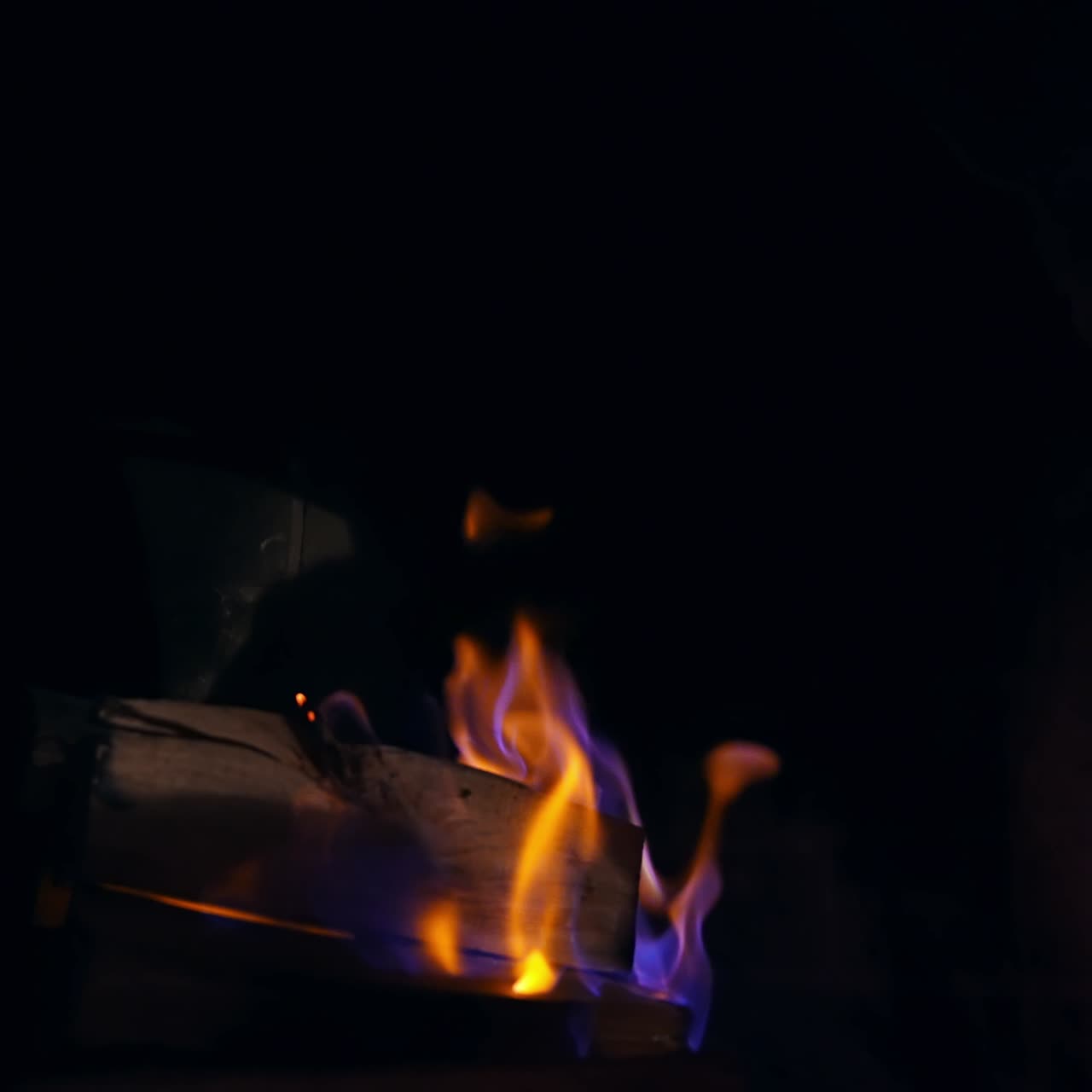 Blue and yellow fire flame burning in a stone fireplace. Wooden logs are burning in darkness. Cozy and warm atmosphere