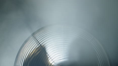 the upper part of a fan rotating in the smoke. the blades cover the spotlight