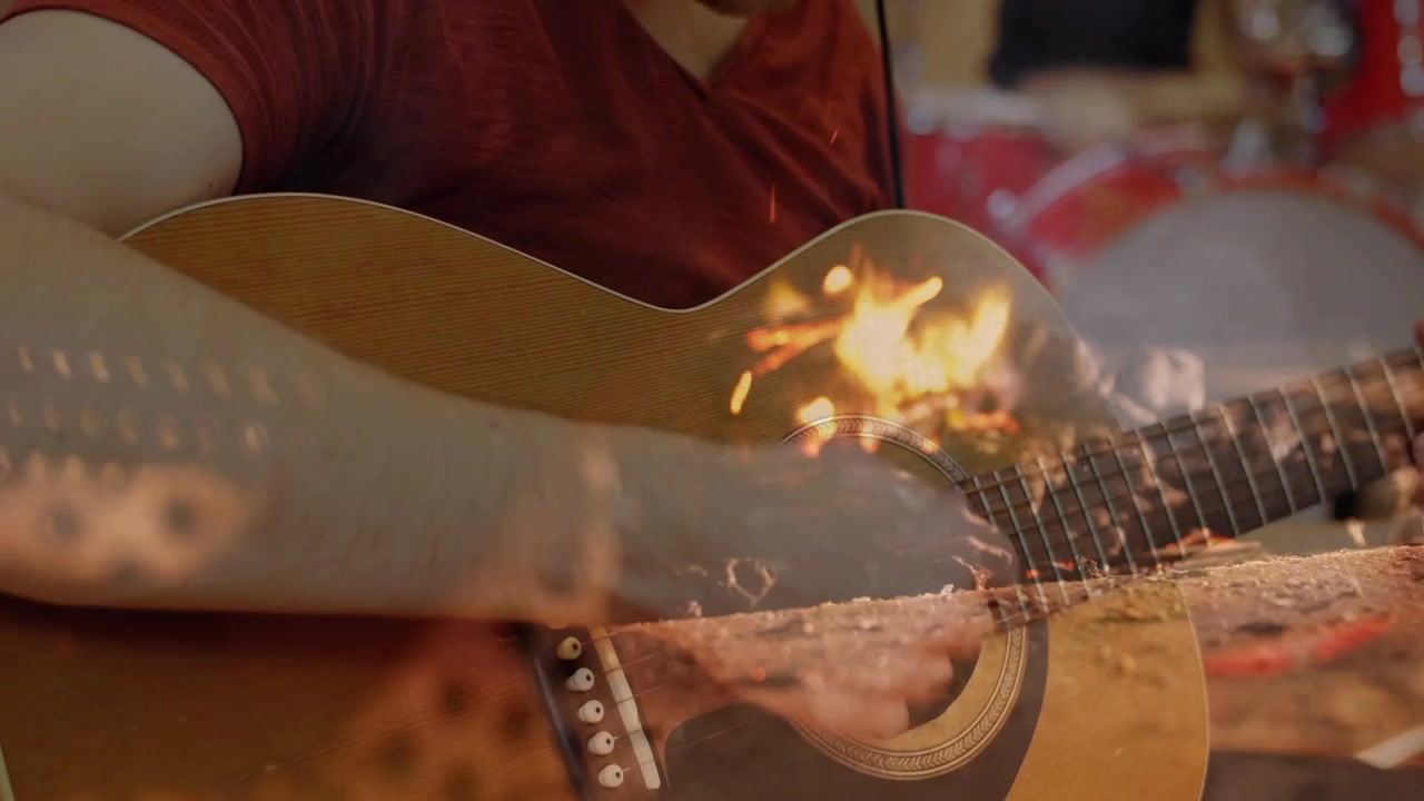 Chitarrista che suona una chitarra acustica generando fiamme mentre un batterista suona i piatti durante una prova musicale.
