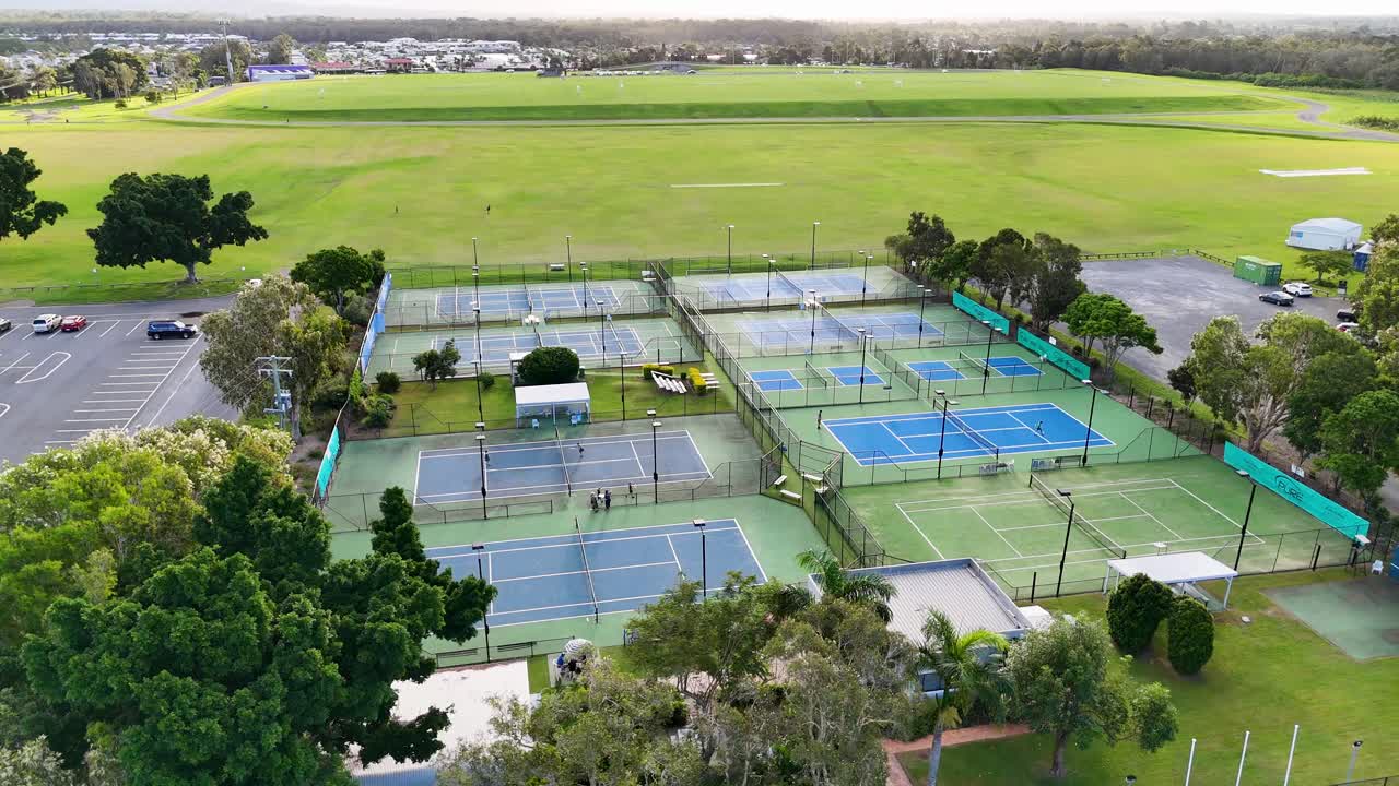 Drone footage captures tennis and pickleball courts surrounded by lush greenery in Gold Coast, Australia, under soft daylight