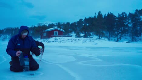 El-Hombre-Con-Su-Perro-Está-Sacando-Agua-De-Un-Agujero-En-El-Lago-Congelado-En-Bessaker,-Condado-De-Trondelag,-Noruega---Toma-Estática