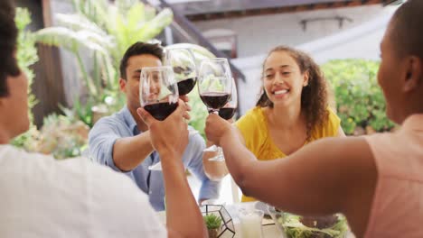 group of diverse male and female friends laughing and toasting with wine at dinner party on patio