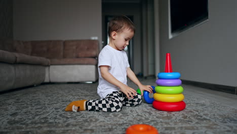 two-year old toddler plays on the floor with his toys. lovely baby building with pyramid.