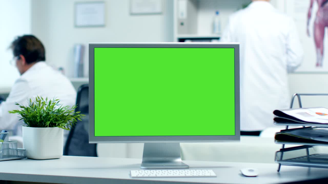 Close-up of a Monitor with Green Screen. Doctor Works with Folders, Assistant Talks with Patients on the Phone. Shot in a Bright and Modern Doctor's Office.