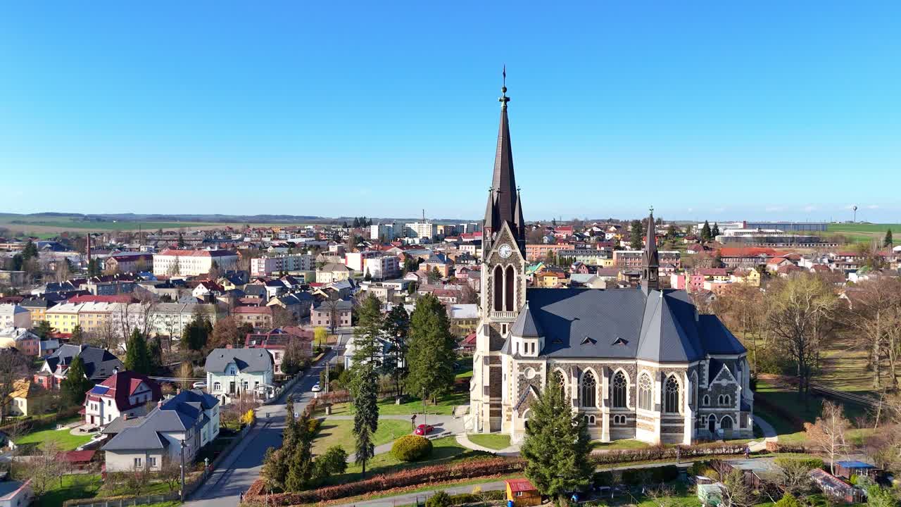 Church spire rises above Vitkov landscape, Czech Republic, surrounded by green spring fields, aerial approach sideview