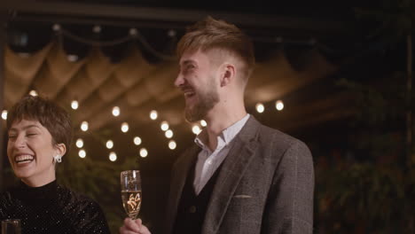 group of four happy multiethnic friends with champagne glasses talking and laughing together at new year's eve party