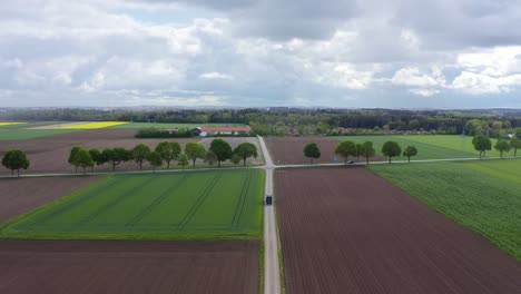 Agricultural-countryside-with-a-driving-tractor-and-the-high-angle-view-of-a-drone-of-flying-backward-over-planted-and-rar-fields