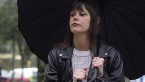 Portrait-of-the-sad,-frustrated-brunette-woman-in-the-black-jacket-under-black-umbrella