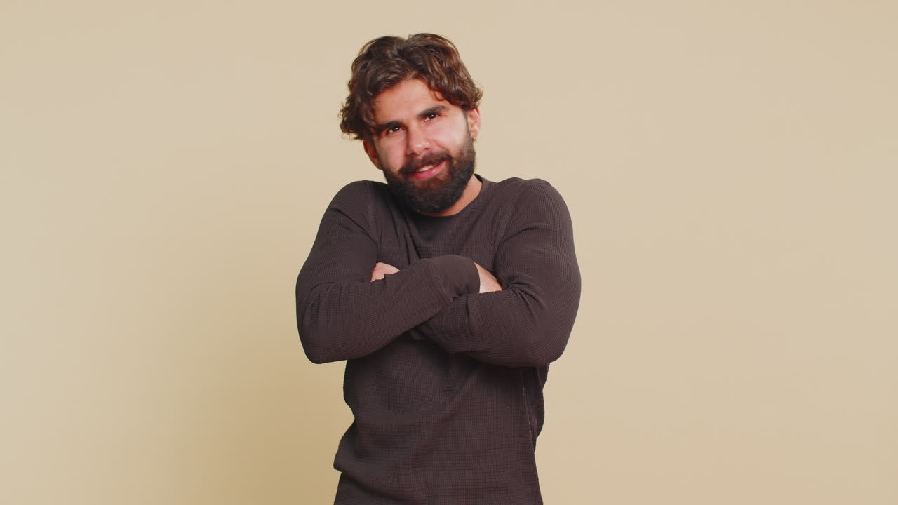 Ritratto di un giovane uomo indiano bello che allarga le braccia per darti un abbraccio, su sfondo beige.