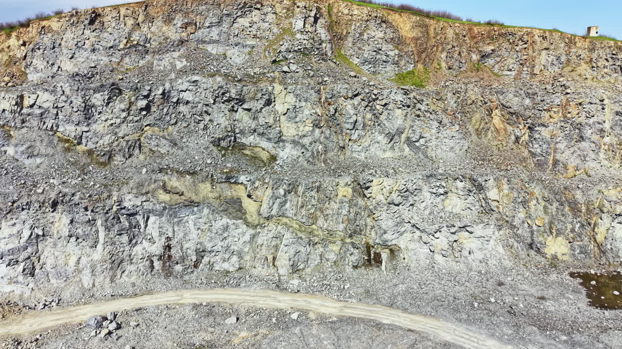 Granitbrud viser lag af sten og klippe med maskineri og arbejdere i aktion nær et mineområde i dagtimerne.