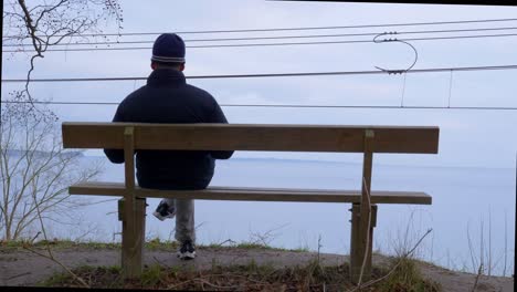 Man-sitting-on-a-bench-overlooking-the-sea,-Handheld