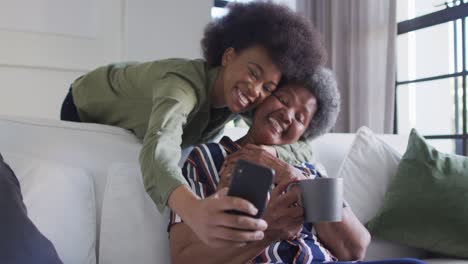 Happy-african-american-adult-daughter-and-senior-mother-taking-selfie-with-smartphone,-slow-motion