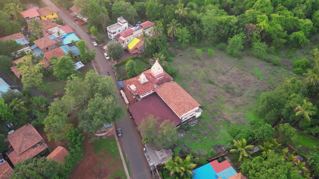A drone shot of Shree Soljai Gramdevi temple in Devrukh, Konkan, Maharashtra, surrounded by lush green trees and houses, with a distinctive round area in front