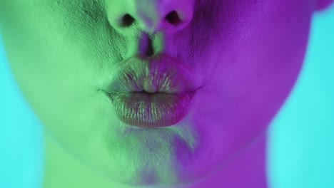 Extreme-close-up-of-beautiful-full-woman-lips-with-applied-lip-gloss-while-she-purses-her-lips-symbolizing-a-kiss-and-then-rejoices-with-green-purple-contrast-in-her-face-in-slow-motion