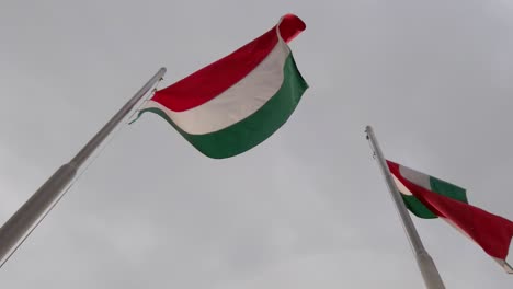 Hungarian-flags-waving-on-flagpoles-with-dark-clouds-in-the-background,-filmed-in-120-fps-slow-motion