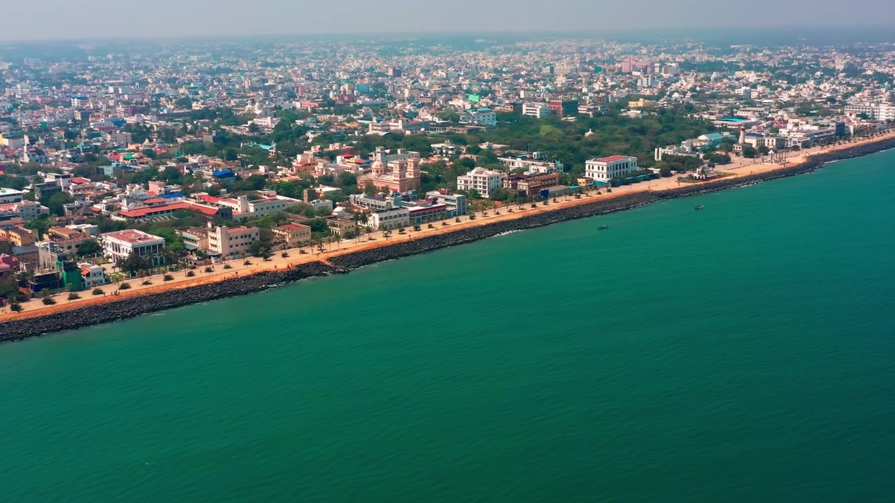 Il lungomare di Goubert Beach Road si estende lungo la costa turchese del Golfo del Bengala a Puducherry, Tamil Nadu. Una vista aerea rivela il viale costiero con barriere rocciose e lo skyline urbano della città.