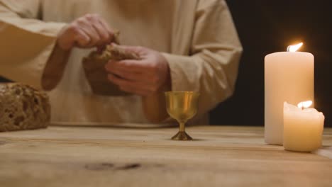 close up shot of man wearing robes representing figure of jesus christ breaking and offering bread