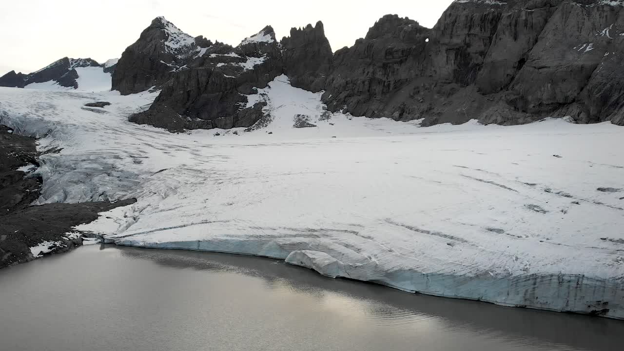 un sobrevuelo aéreo giratorio sobre el lago glacial del glaciar claridenfirn en uri, suiza al anochecer con una vista del cielo brillante detrás de los picos alpinos y los icebergs flotantes en el agua