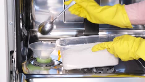 A Woman Adds Salt to the Detergent Solution in the Dishwasher Using a Special Vessel. A woman adds salt to the detergent solution in the dishwasher using a special vessel. Adding salt, increasing the efficiency of the dishwashing process. Salt helps to achieve an attractive appearance of dishes