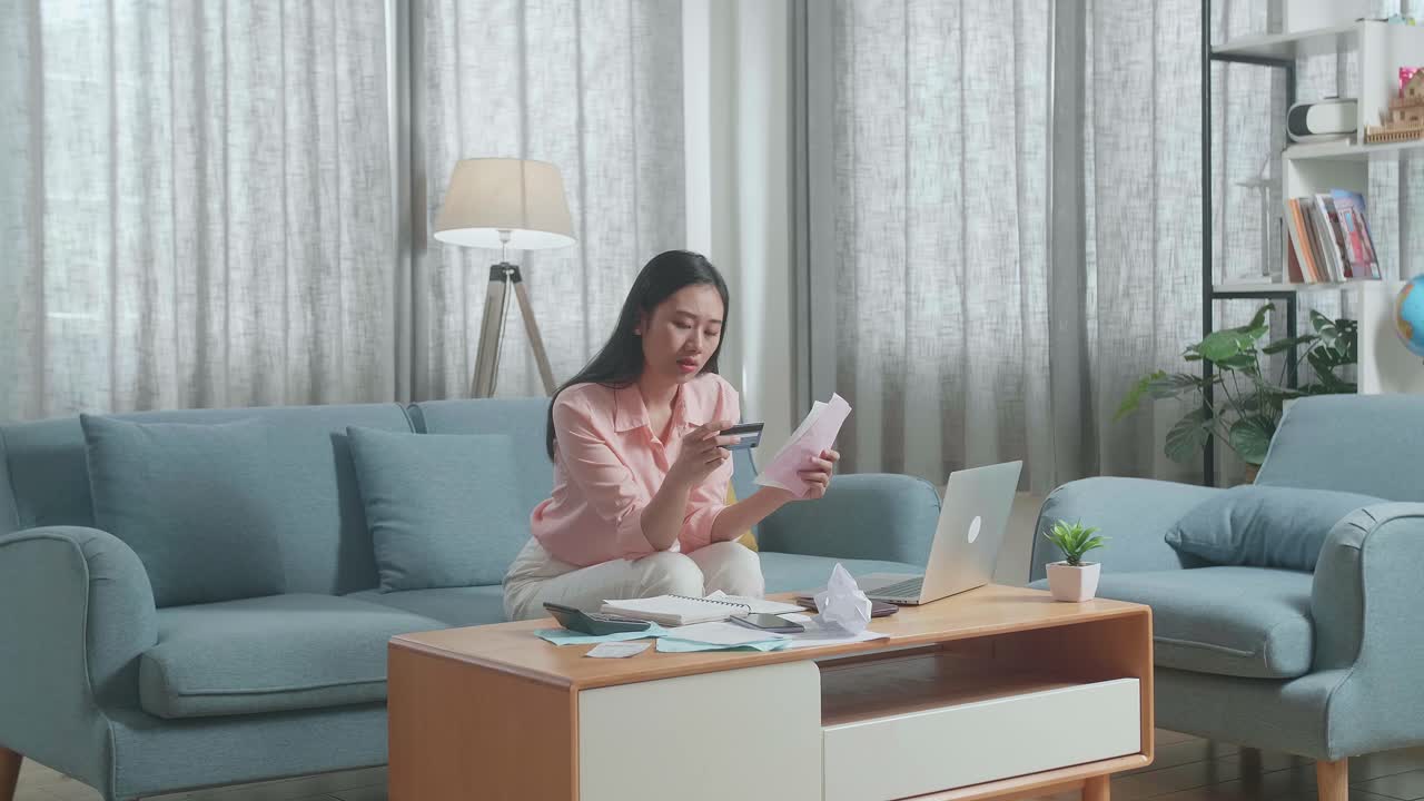 노트북을 가진 아시아 여성이 청구서와 신용카드를 보고 머리를 흔들고 두통을 고 있습니다.