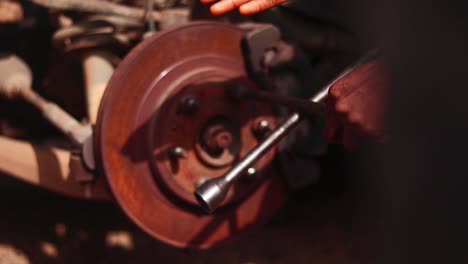fixed camera close-up of a mechanic’s hand using a tool on a rusted car brake in nigeria.
