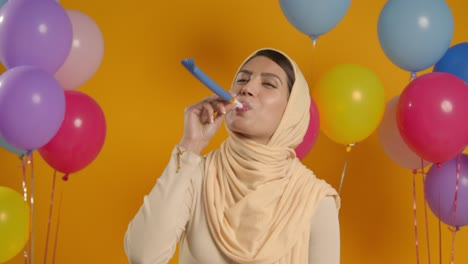 studio portrait of woman wearing hijab celebrating birthday with balloons and party blower