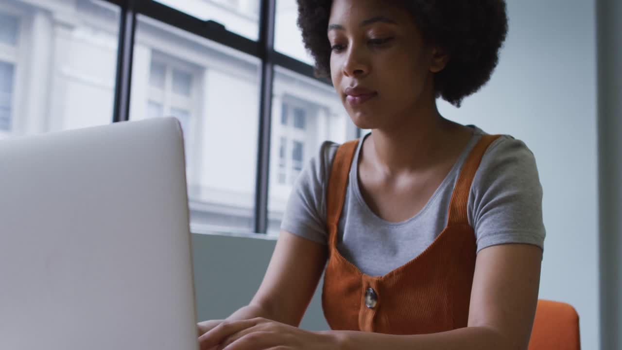 Mixed race businesswoman sitting and using a laptop in modern office