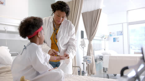 african american female doctor examining girl using stethoscope in hospital room, slow motion