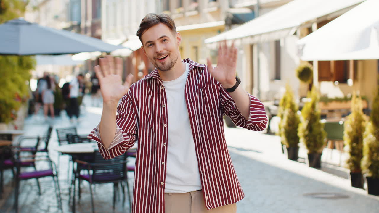 joven sonriendo amistosamente a la cámara agitando las manos hola hola saludo o adiós en la calle de la ciudad